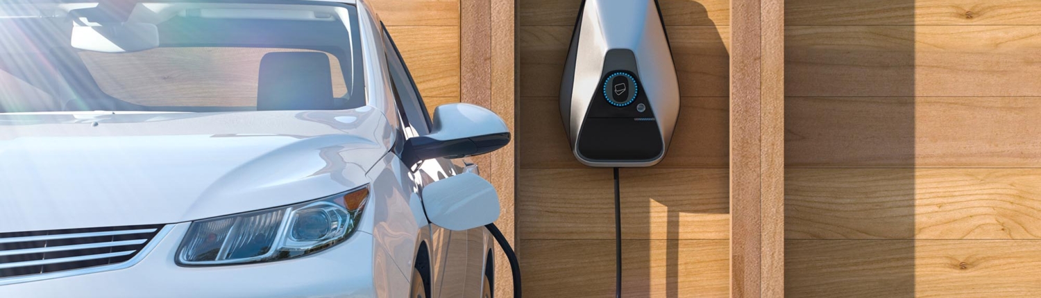 Front view of an electrical car charger mounted to a wooden wall plugged in to a white sedan